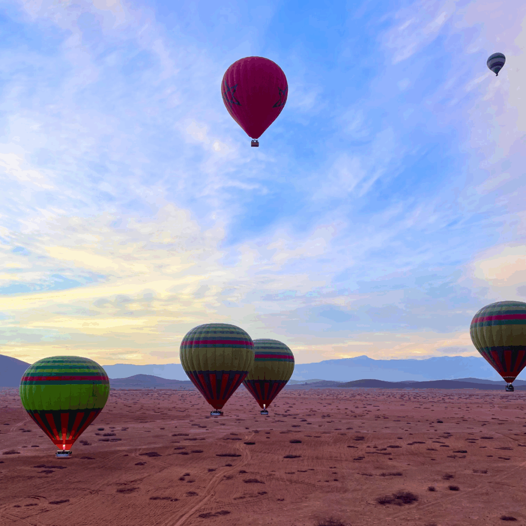 Hot air balloons float with the high atlas mountains in the backgrond